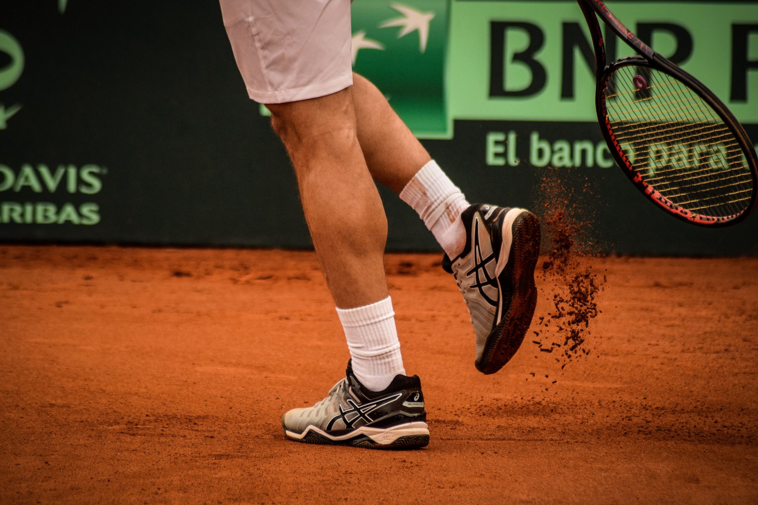 tennisman frappant ses chaussures avec sa raquette pour enlever le sable